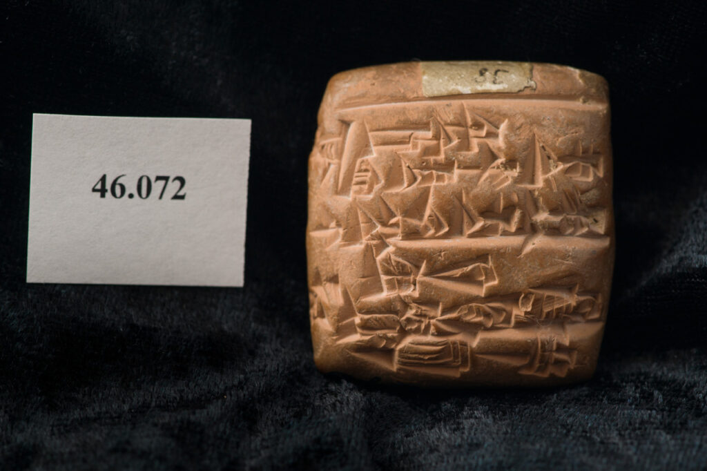 Square clay block with intricate carvings on surface sitting on dark fabric.