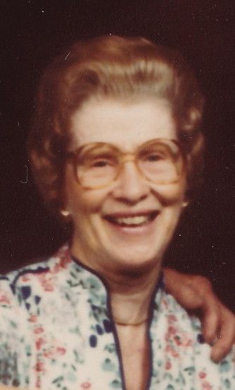 Color headshot of Clara Cassity wearing a colorful white and dotted print shirt, glasses, and with hair slightly smoothed back. A hand is on her left shoulder, but the other person is unseen.